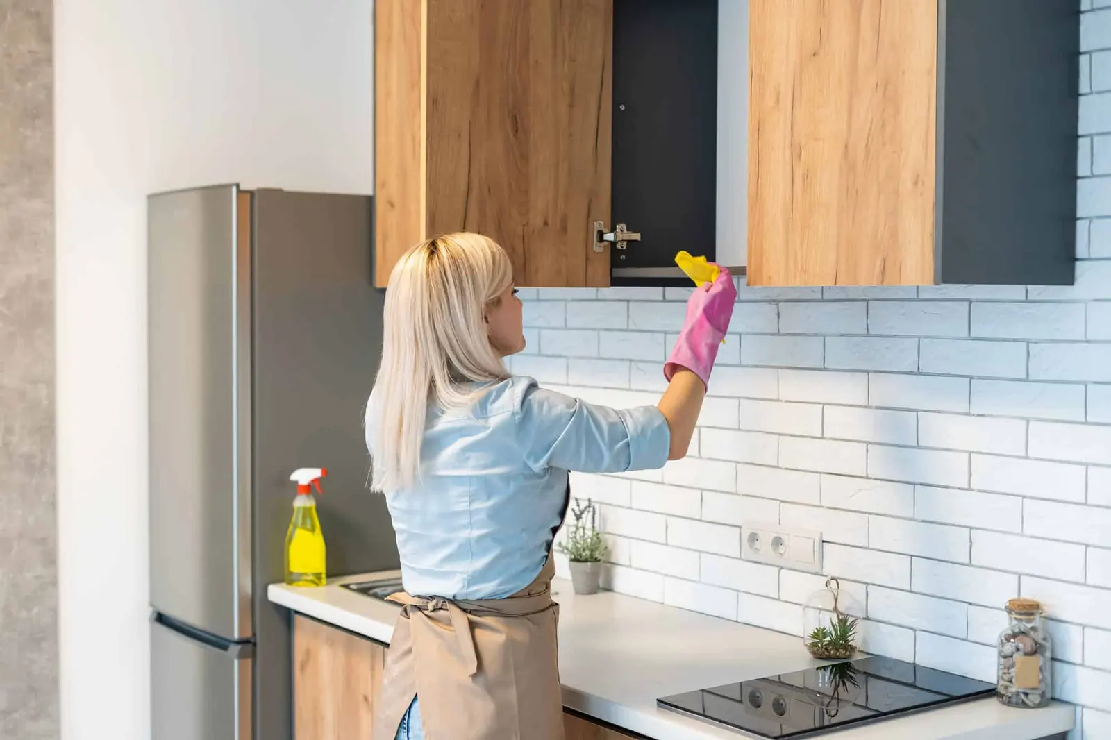 A person wiping down a wooden kitchen cabinet door with a cloth